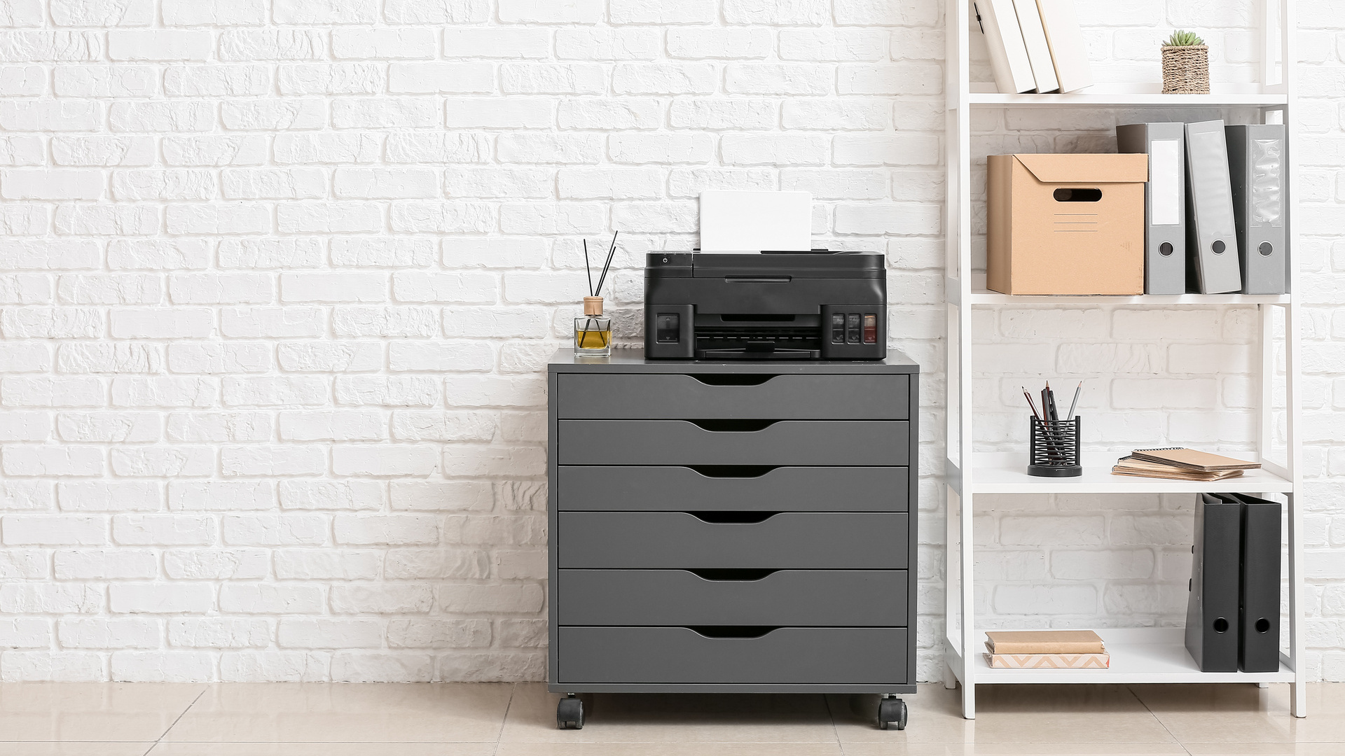 Chest of drawers wiht modern printer and shelf unti in front of a white brick wall