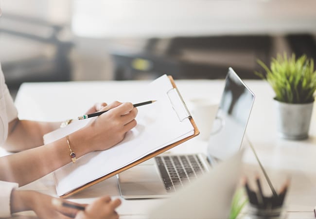 Woman holding a checklist with client in front of a laptop
